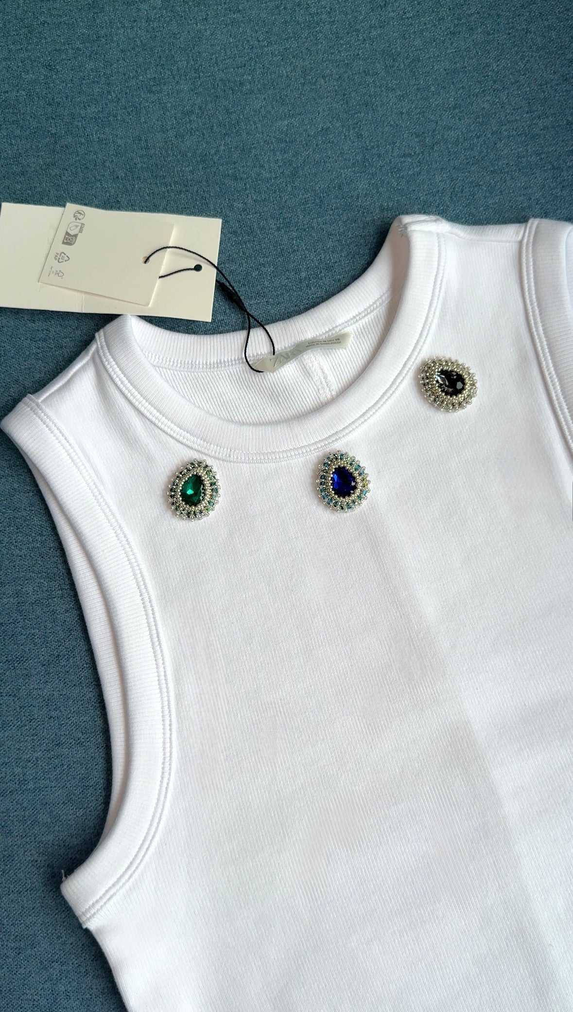 White ribbed sleeveless top with green, blue and dark green teardrop gemstone embellishments near the neckline