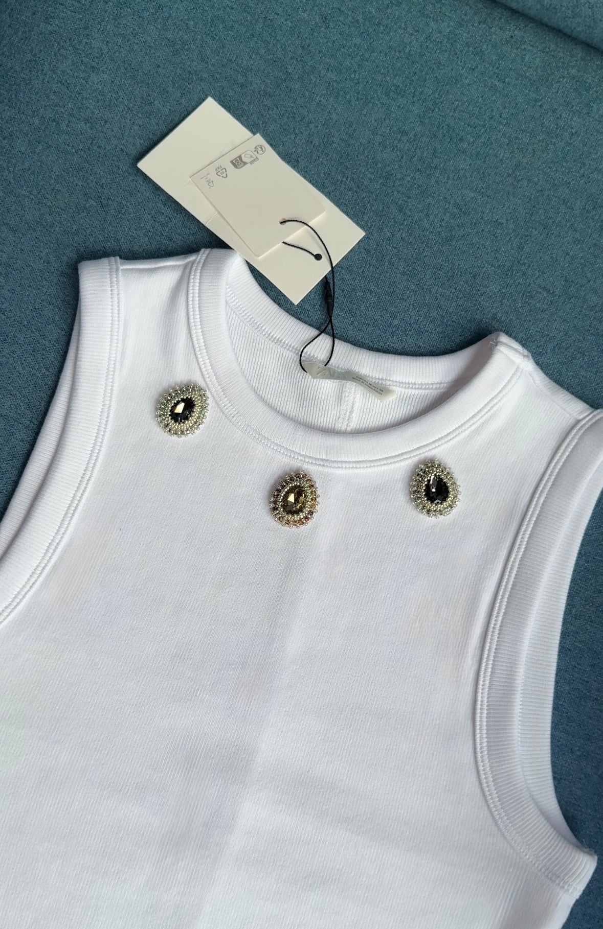 White ribbed sleeveless top with three dark green and olive gemstone embellishments near the neckline