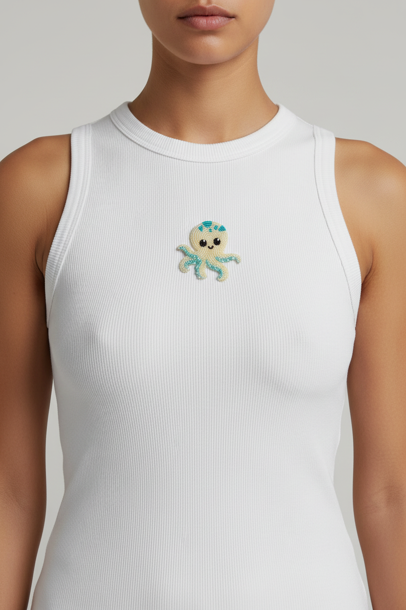Close-up of the white ribbed top showing the handmade yellow and turquoise beaded octopus motif, thick neckline, and wide armhole binding