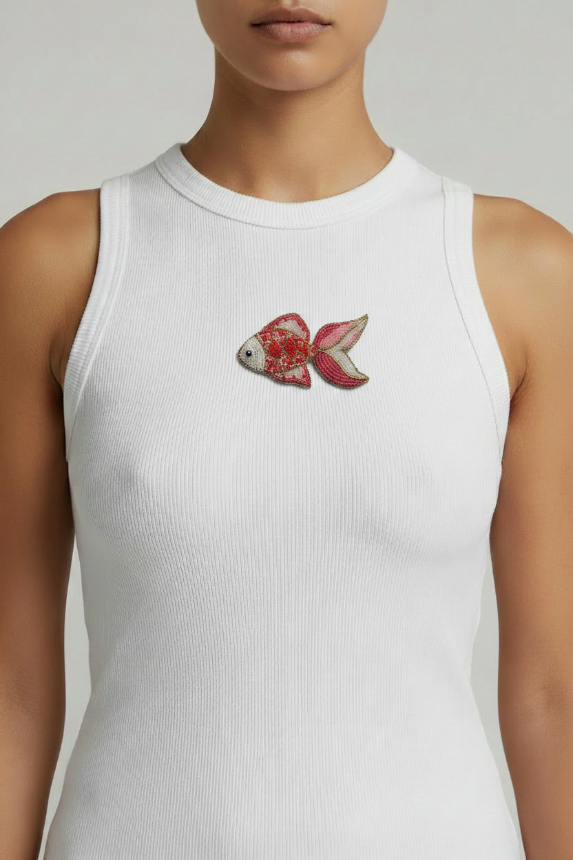 Close-up of handmade pink fish beadwork sewn onto white ribbed top fabric